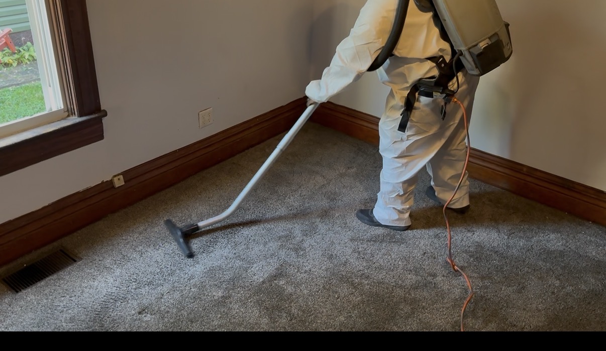 Technician in protective suit HEPA vacuuming carpet during mold remediation